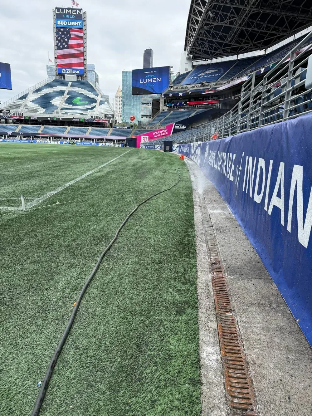 The drainage channel running along the edge of the pitch at Lumen Field, with the jetting hose run out along the touchline.