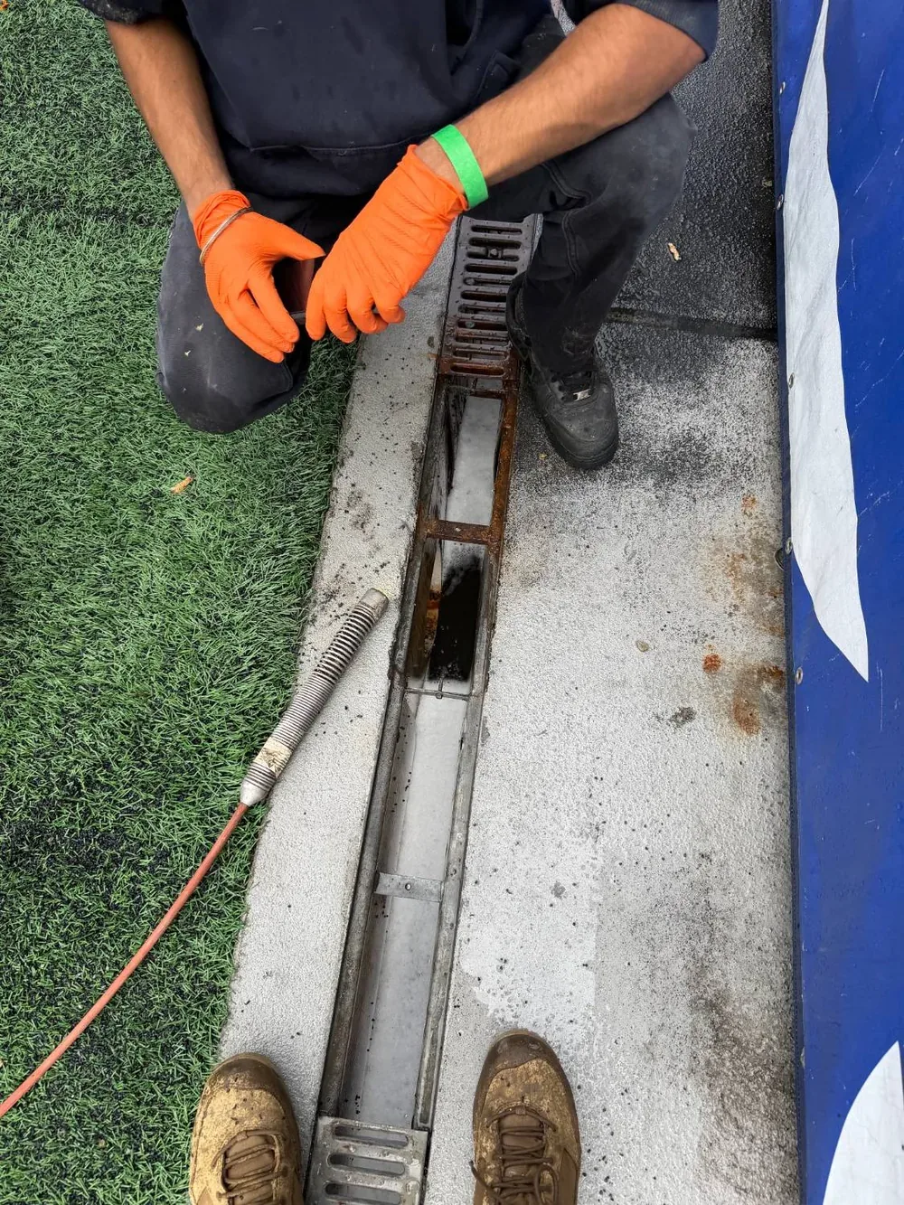 The french drain with its cover removed, showing the open channel and standing effluent.