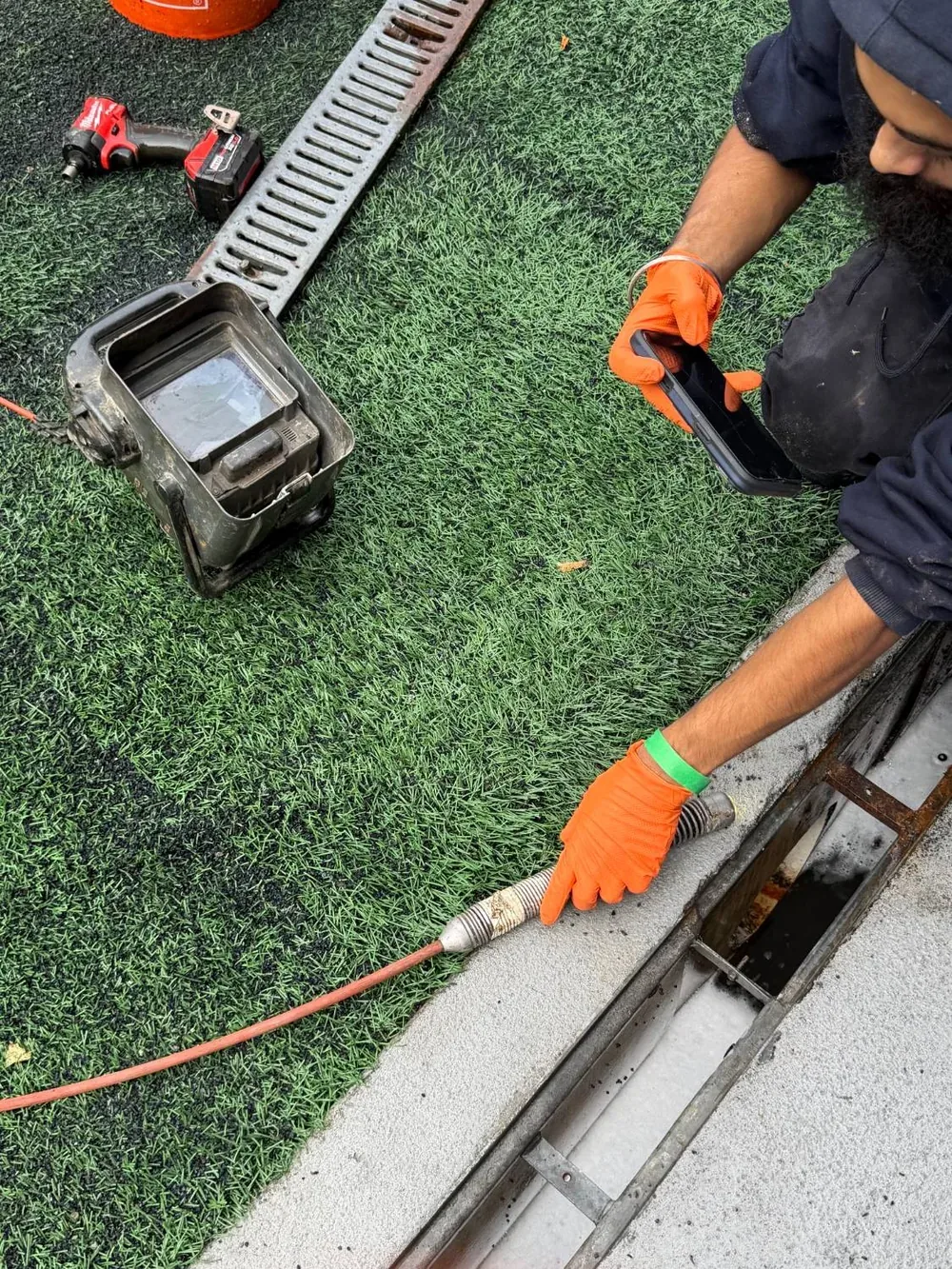 A jetting hose fed into the open drain, with the equipment set up on the turf alongside.