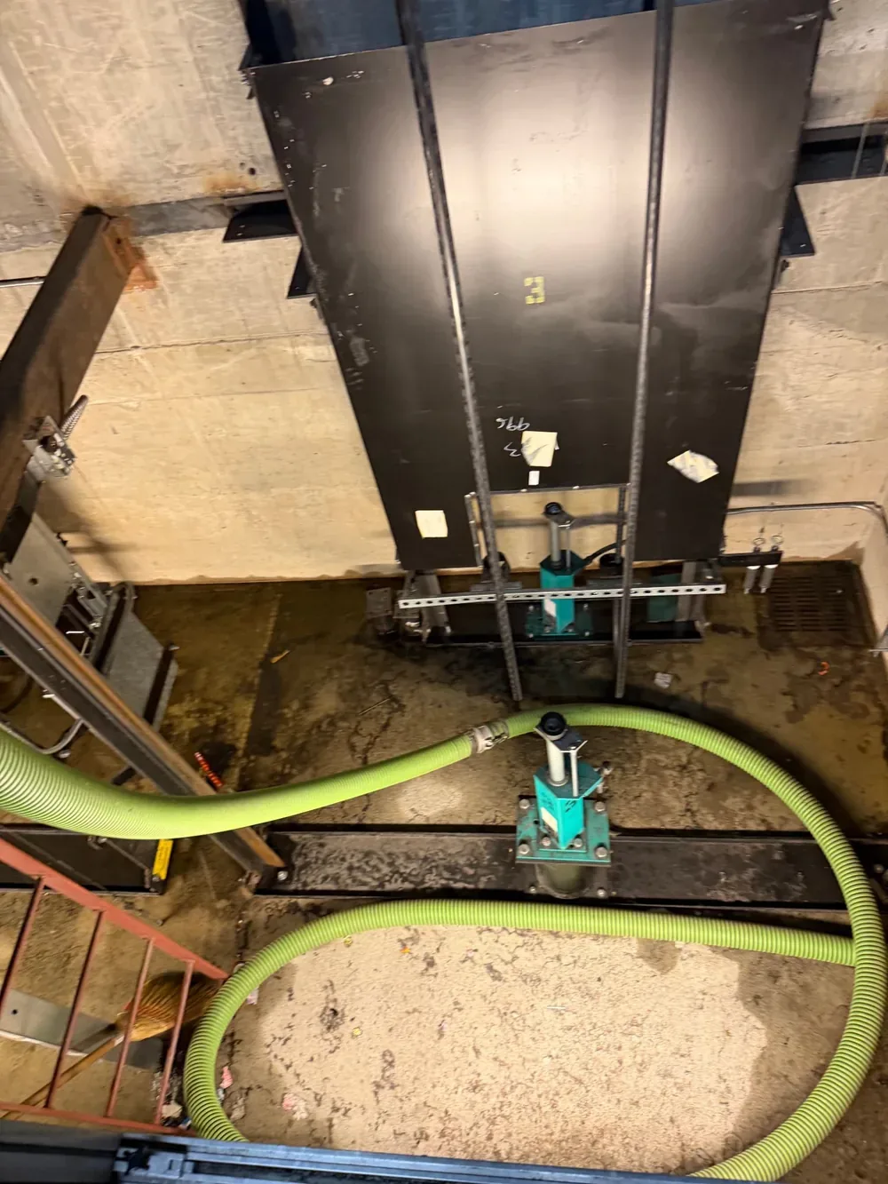 Looking down into the elevator pit, with the suction hose in place beside the buffer and guide rails.