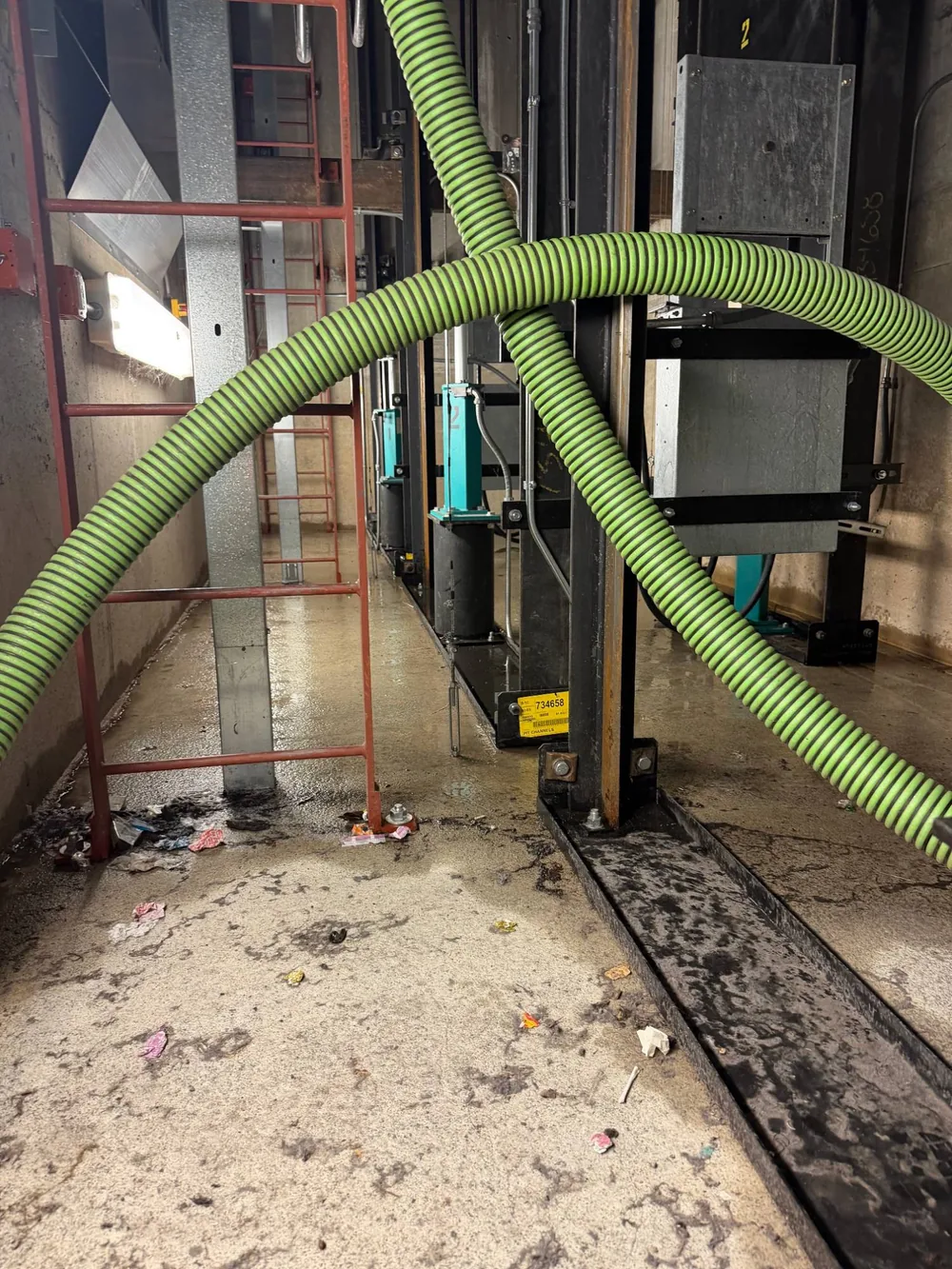 Suction hoses running through the elevator pit area, with water and debris across the floor.