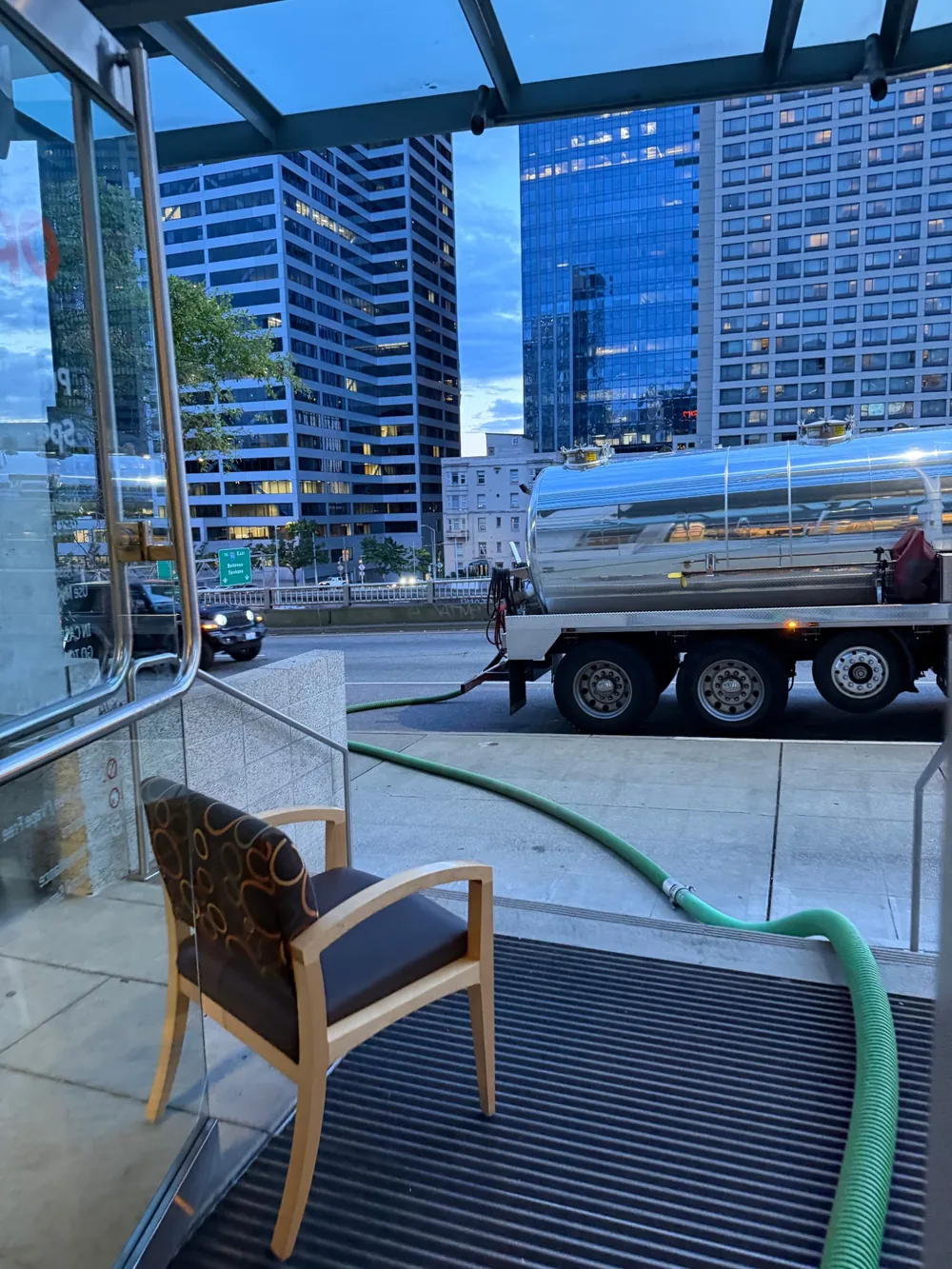 The vacuum truck on the street seen from just inside the building entrance, with the suction hose running in across the pavement.