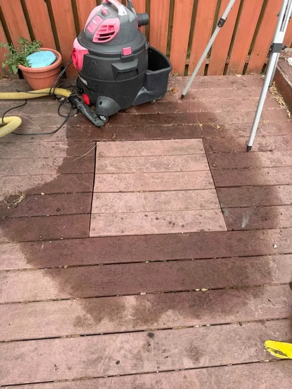 A section of decking lifted clear of the septic lid, with a wet patch spread across the surrounding boards and a vacuum unit and hoses set up alongside.