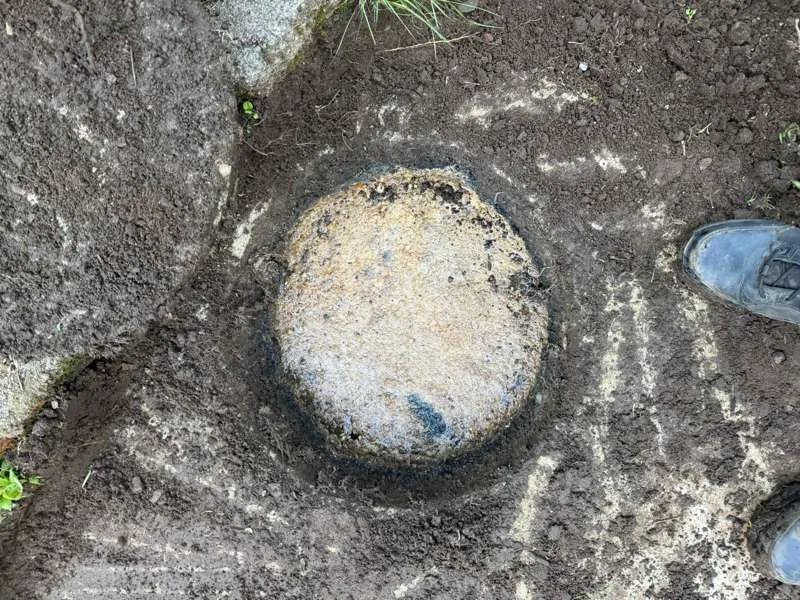 A tank access lid seated at grade, crusted over.