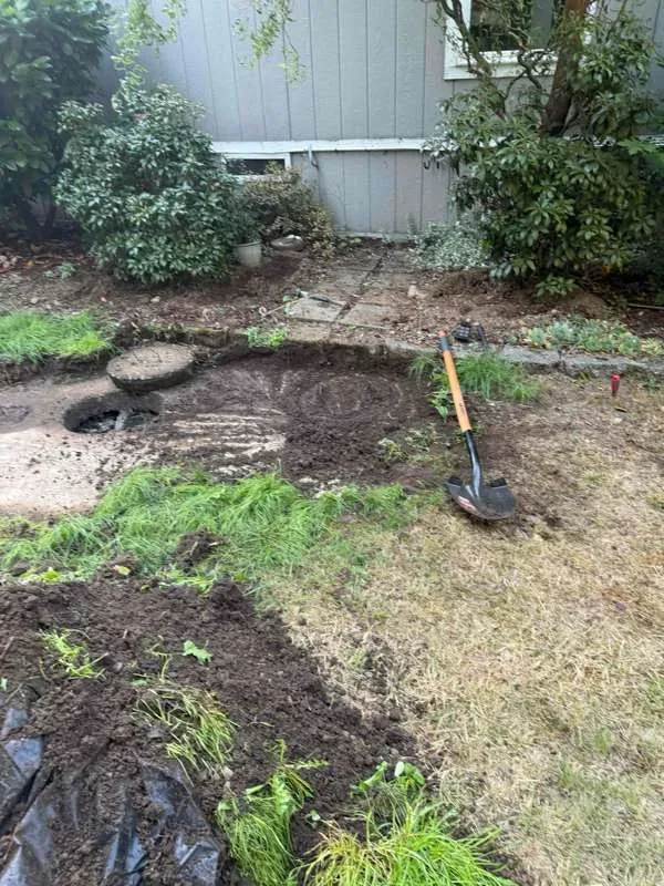 The work area in the back garden beside the house, with the ground opened up and a shovel resting alongside.