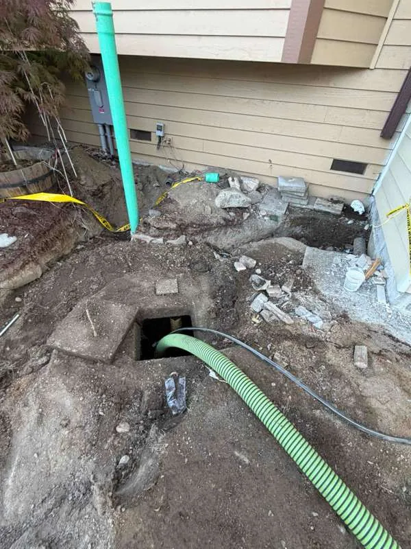 The excavation alongside the house, taped off, with the lid slabs set aside on the dirt.