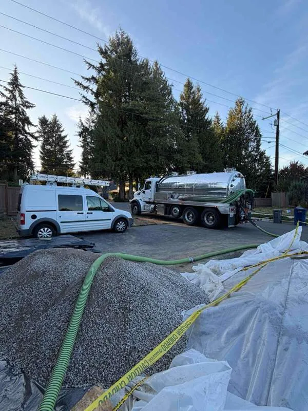 The vacuum truck and service van at the kerb, with the suction hose run in over the gravel.