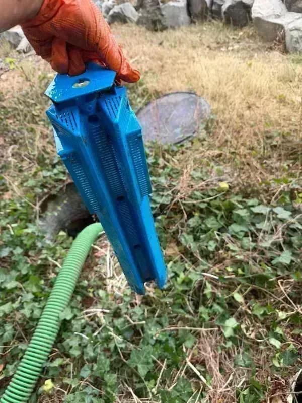 A blue slotted effluent filter cartridge lifted out and held above the tank.