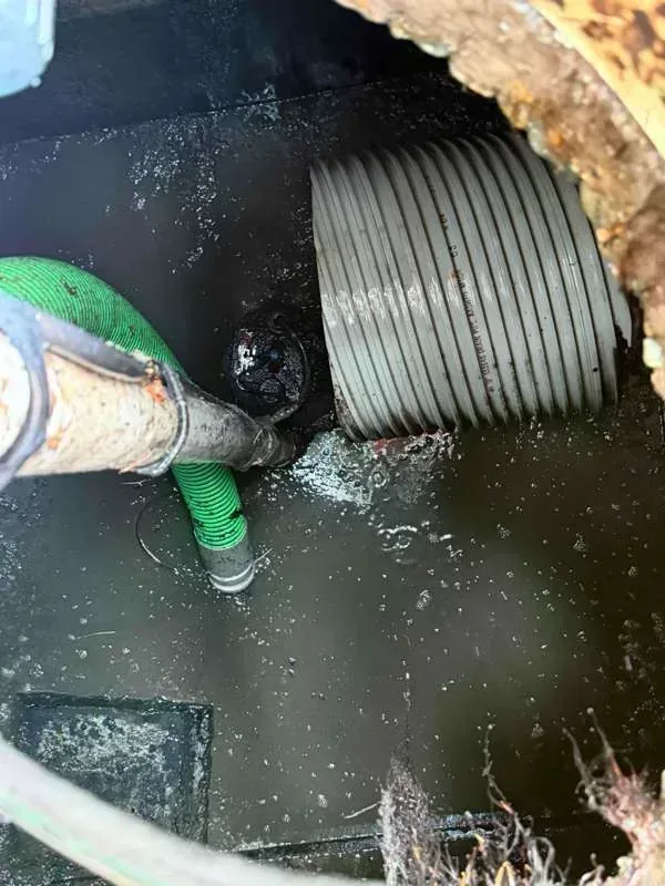 Inside the tank during pumping, with the suction hose alongside a large corrugated pipe entering the wall.
