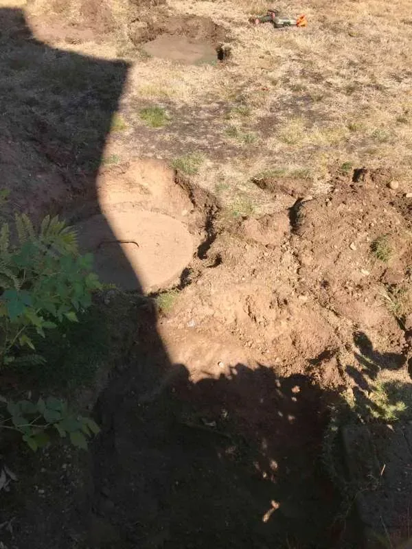 The ground opened up around a tank lid, with tools set out on the grass.