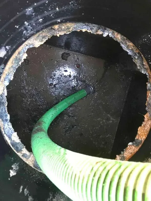 Looking down a riser at the tank top with the suction hose in place, the riser rim heavily scaled.
