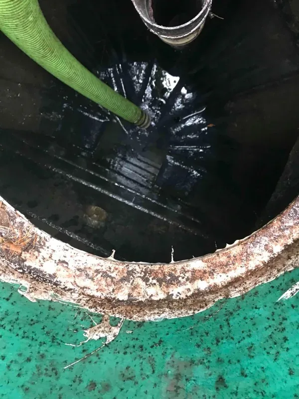 A tank chamber part-pumped, with the suction hose running in and the concrete lid seat visible around the opening.