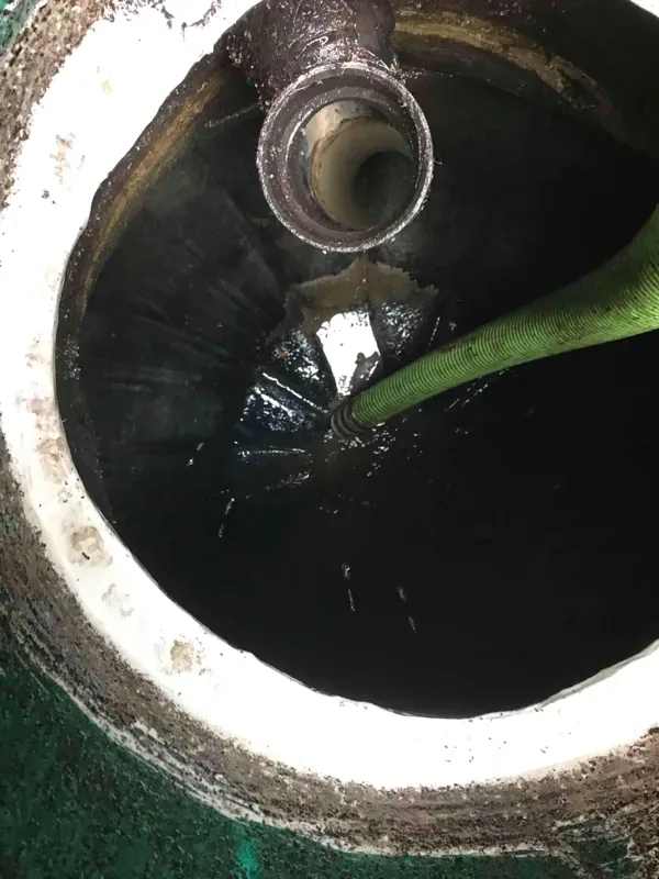 Looking down into the septic tank as it is pumped, with the suction hose in place and a pipe entering at the top.