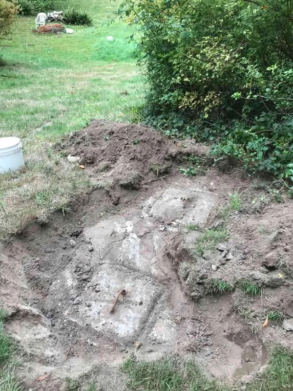 The tank exposed in the back garden, both access lids uncovered, with the excavated soil heaped alongside.