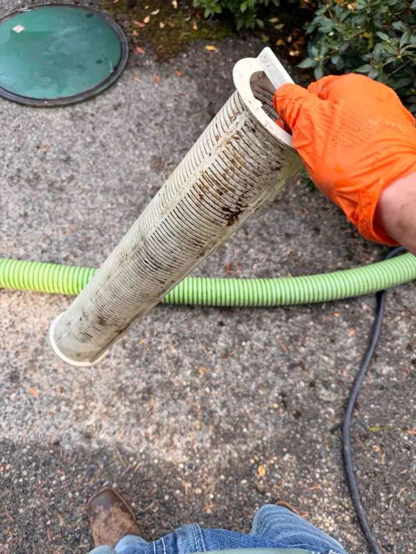 An outlet baffle filter after cleaning, set down on the driveway beside the hose.