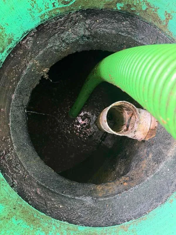 The suction hose lowered through a riser into the flooded tank, with the pipe stub visible alongside.