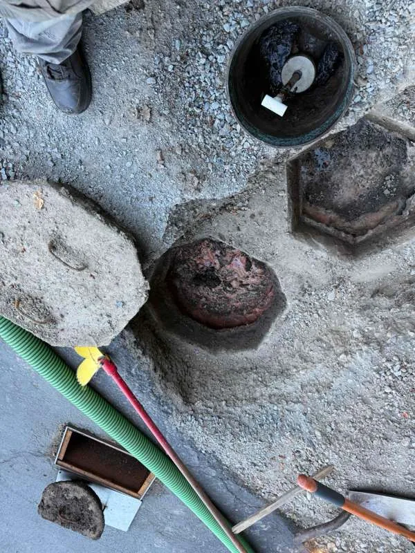 The tank openings in the gravel, with tools and the suction hose laid alongside.