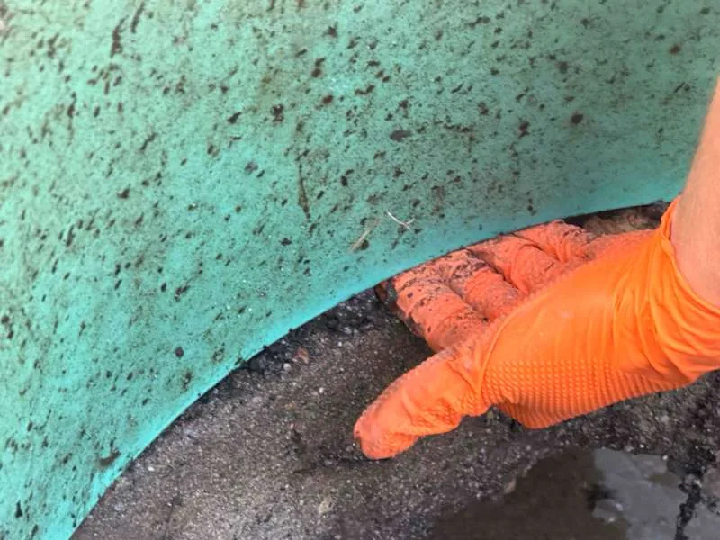 A gloved hand in the gap where the riser meets the top of the tank.