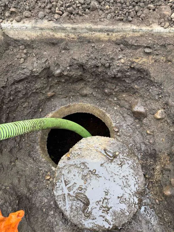 A concrete lid slid back off the access opening with the suction hose fed in beside it.