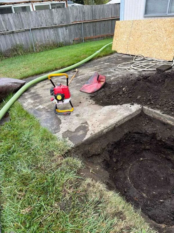 The work area in the back garden, with both tank compartments excavated and the suction hose run out across the lawn.