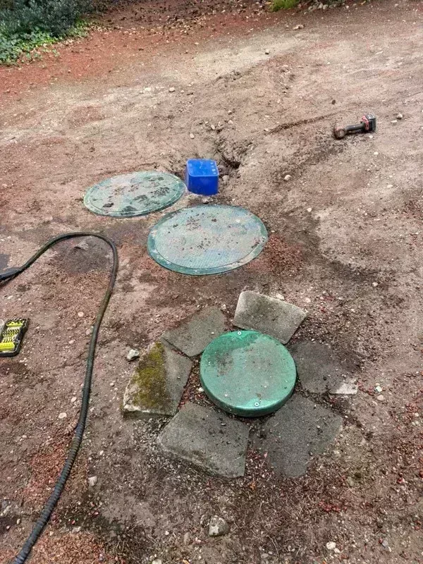 Two access lids lifted and laid on the ground, with a third still seated in its concrete surround.