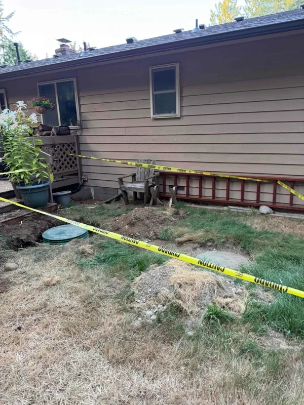 The excavation alongside the house, with the chamber lids exposed inside the taped area.