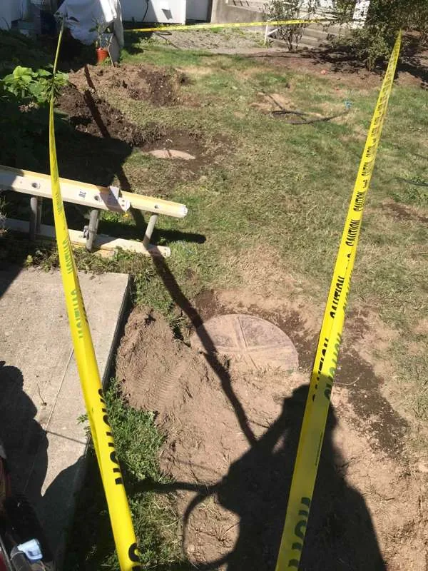 The excavation taped off for safety, with two of the riser lids uncovered at the edge of the patio.