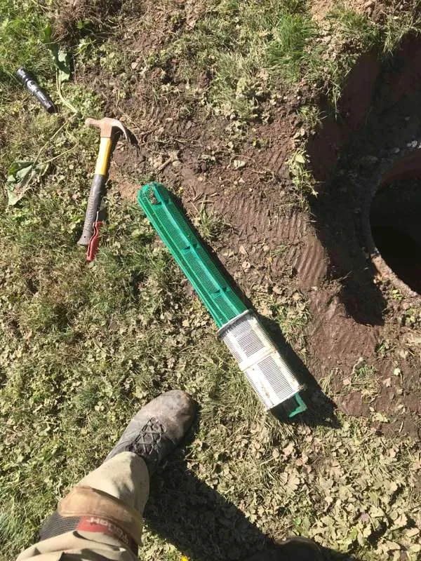 The outlet baffle filter set down on the grass beside the open riser.