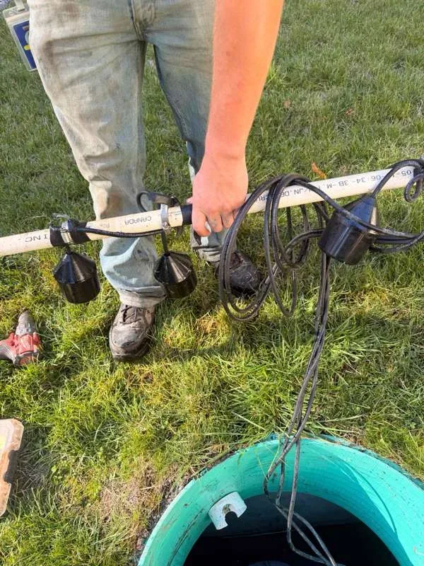 A technician holding the float assembly up out of the pump tank riser, floats and cords clear of the opening.