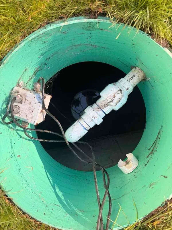 Looking down into the pump tank riser at the discharge plumbing and the junction box on the wall.