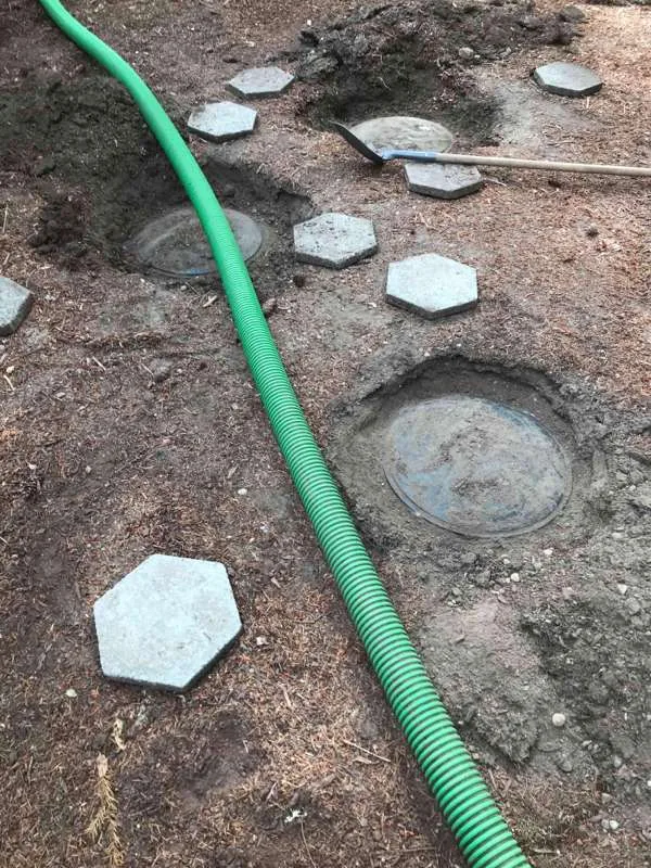 The suction hose run across the yard to the uncovered tank lids, stepping stones lifted aside.