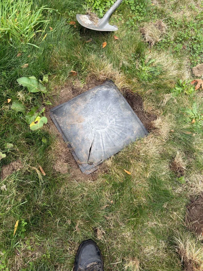 The cracked lid found during the inspection, set flush in the lawn with a shovel alongside.