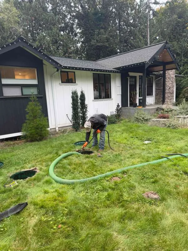A technician working at an open riser, with the suction hose run back across the lawn.