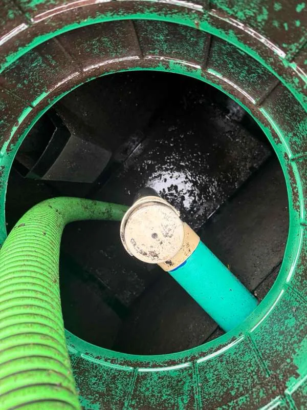 Looking down a green riser at the tank, with the suction hose and the outlet pipe below.