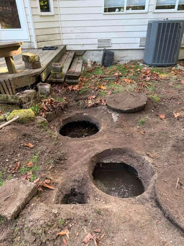The back of the house with two access openings excavated down to the tank and a concrete lid set aside on the ground.