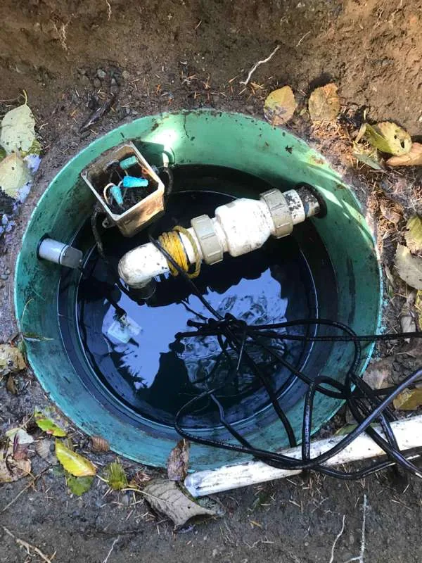 Looking down the riser at the flooded pump tank, with the pump pipework, a junction box and cables above the waterline.