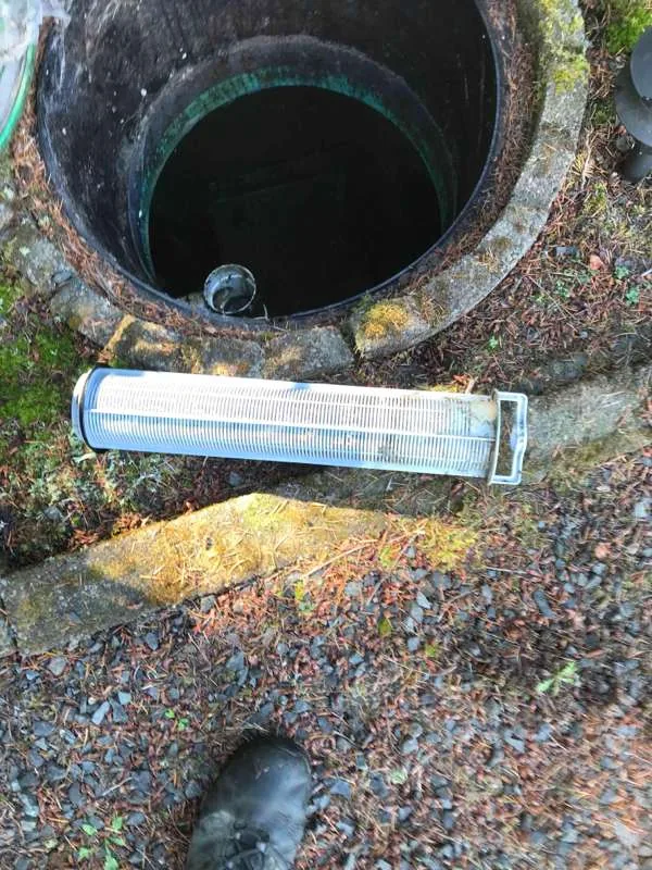 The cylindrical effluent filter cartridge pulled out and laid on the ground beside the open riser.