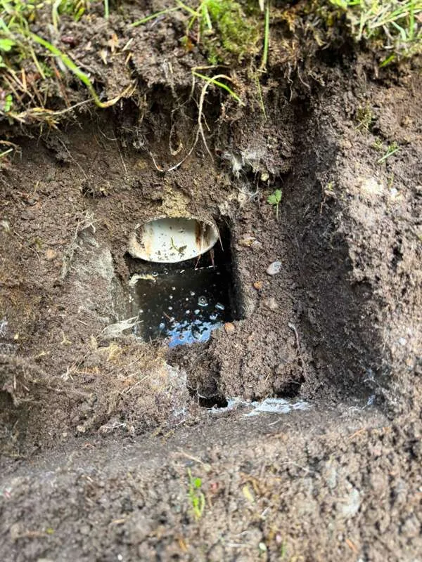 A white pipe end exposed in a dug pocket at the side of the tank.