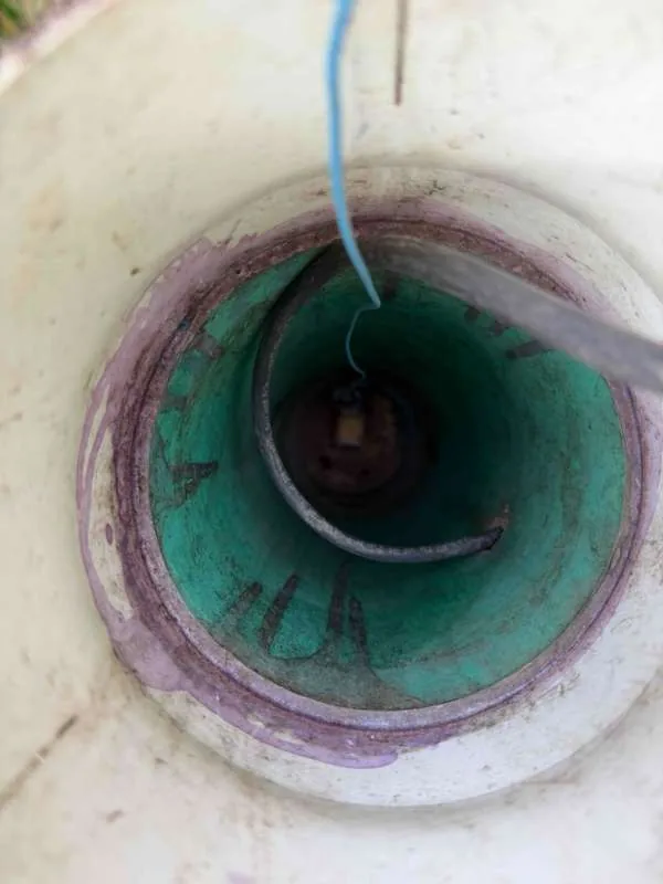 Looking down an access riser at the green inner pipe below, with a cable and a lifting hook running down into it.