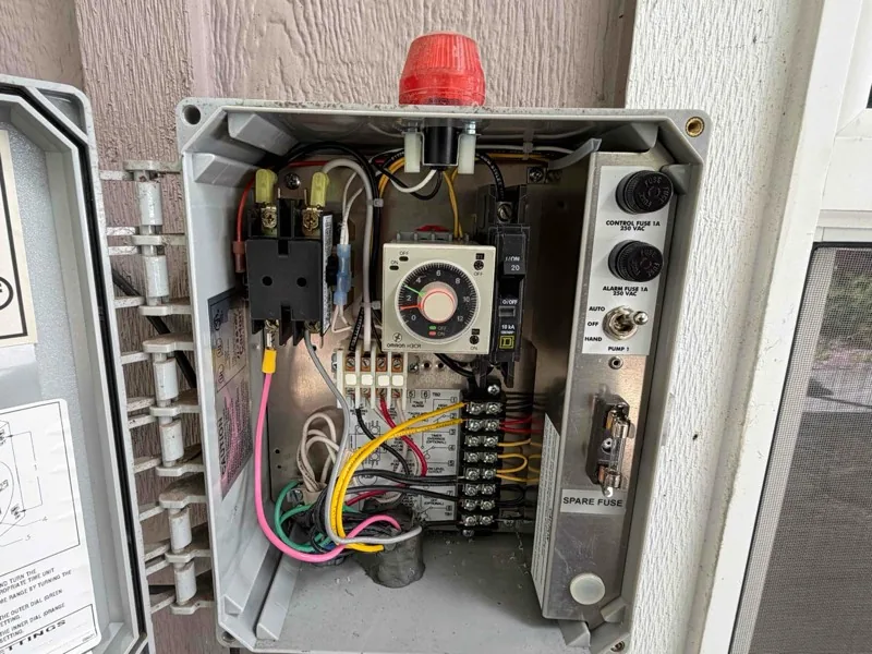 The open control panel on the house wall, showing the timer, the breakers and the alarm beacon.