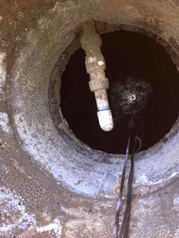Looking down the concrete pump tank riser at the discharge plumbing and a float cord.