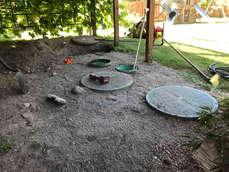 The uncovered lids in the dug-out ground beside the play structure, with tools set down on one of the concrete lids.