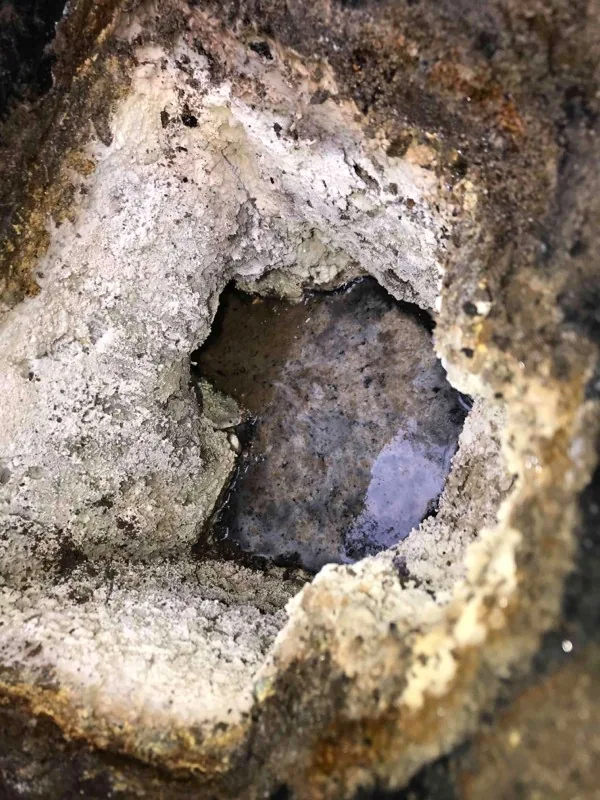 A heavily crusted opening in the tank, with liquid standing behind it.