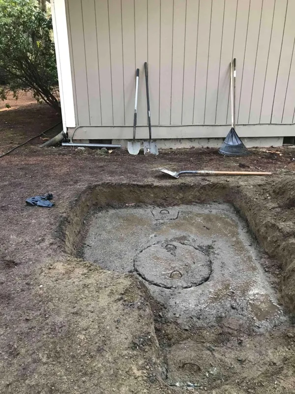 The tank dug out beside the building, with tools leaning against the wall behind it.