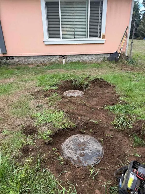 Two tank lids uncovered in the lawn beside the house, with the turf cut back around them.