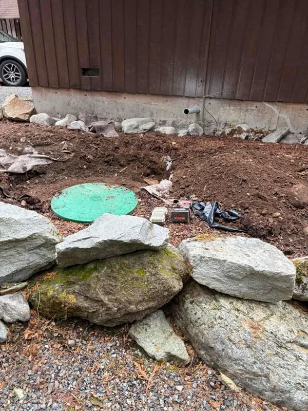 The excavated area beside the cabin, with a riser lid in the ground and tools laid out around it.