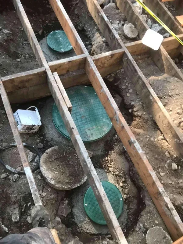 Riser lids set into the ground beneath the opened deck framing.