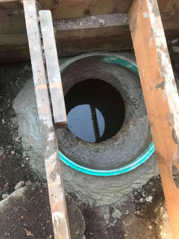 A riser collar set in fresh concrete over a tank opening, with liquid below.