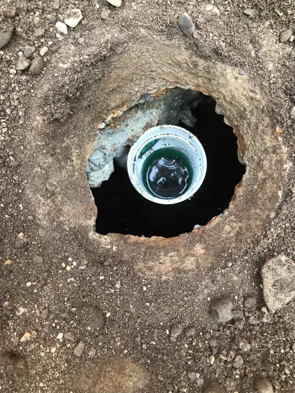 Looking down a dug-out opening at a pipe end below.