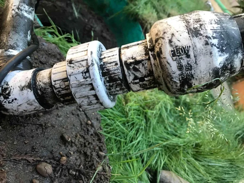Close-up of the discharge pipe fittings, with the check valve marked FLOW and THIS SIDE UP.
